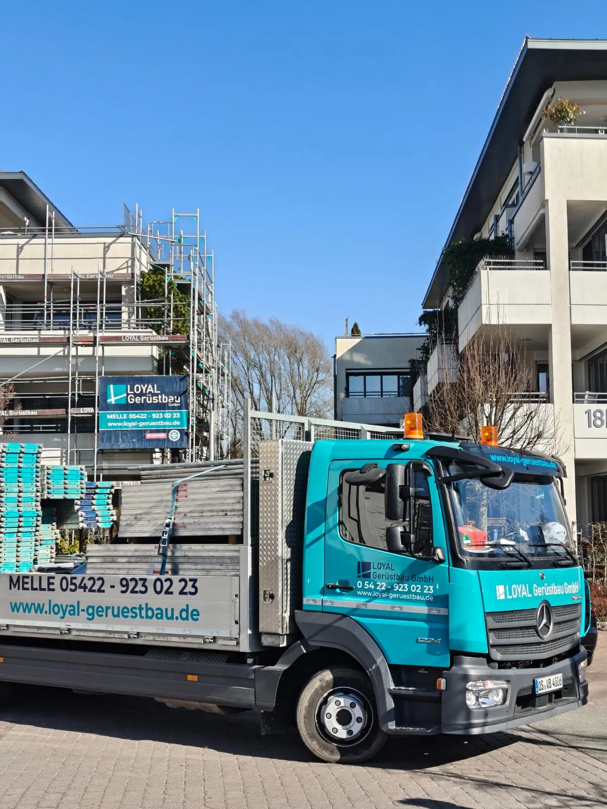 Türkiser LOYAL Lkw vor einer eingerüsteten Baustelle